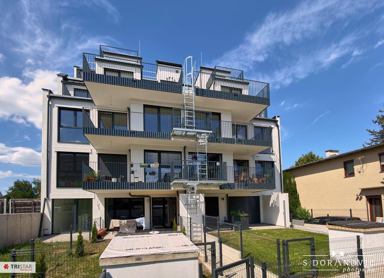 Fassade des Neubaus mit mehreren Etagen, Balkonen und einer markanten Außentreppe.