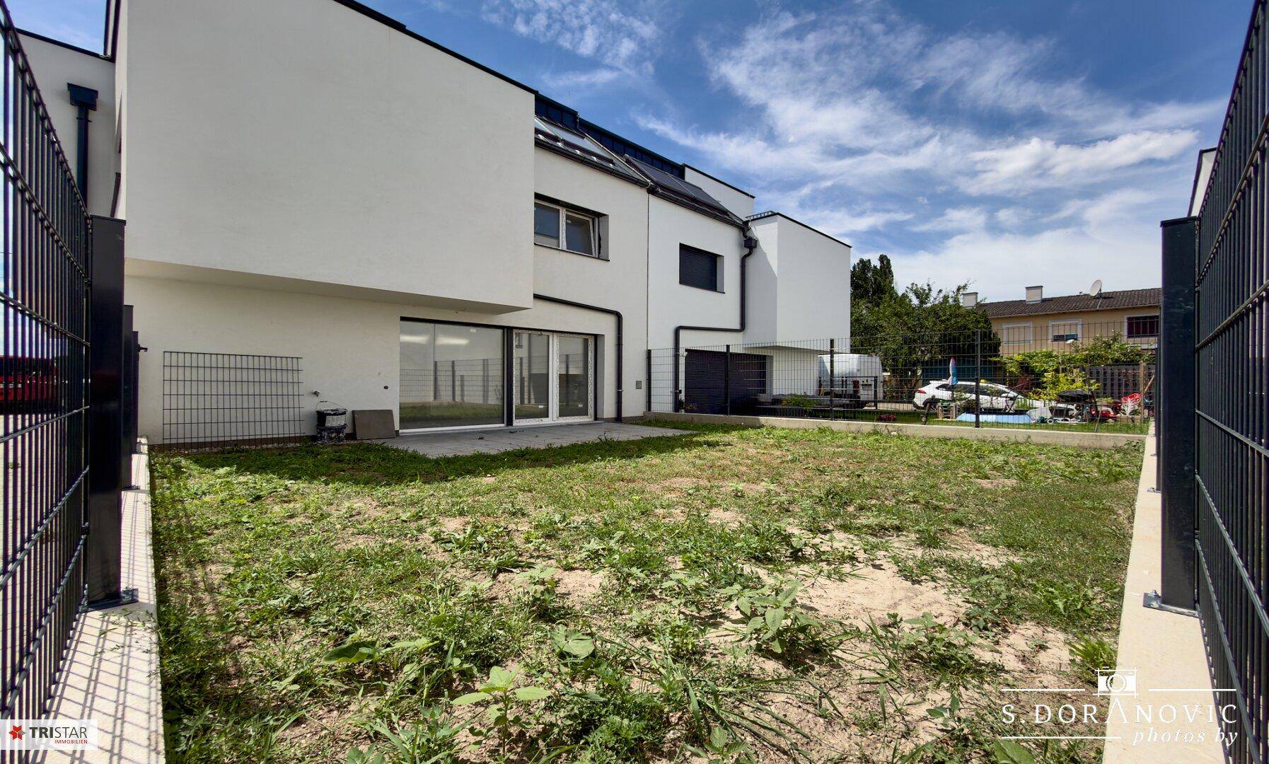 Hinterer Gartenbereich eines modernen Neubaus mit Rasenfläche und großen Glasfronten.