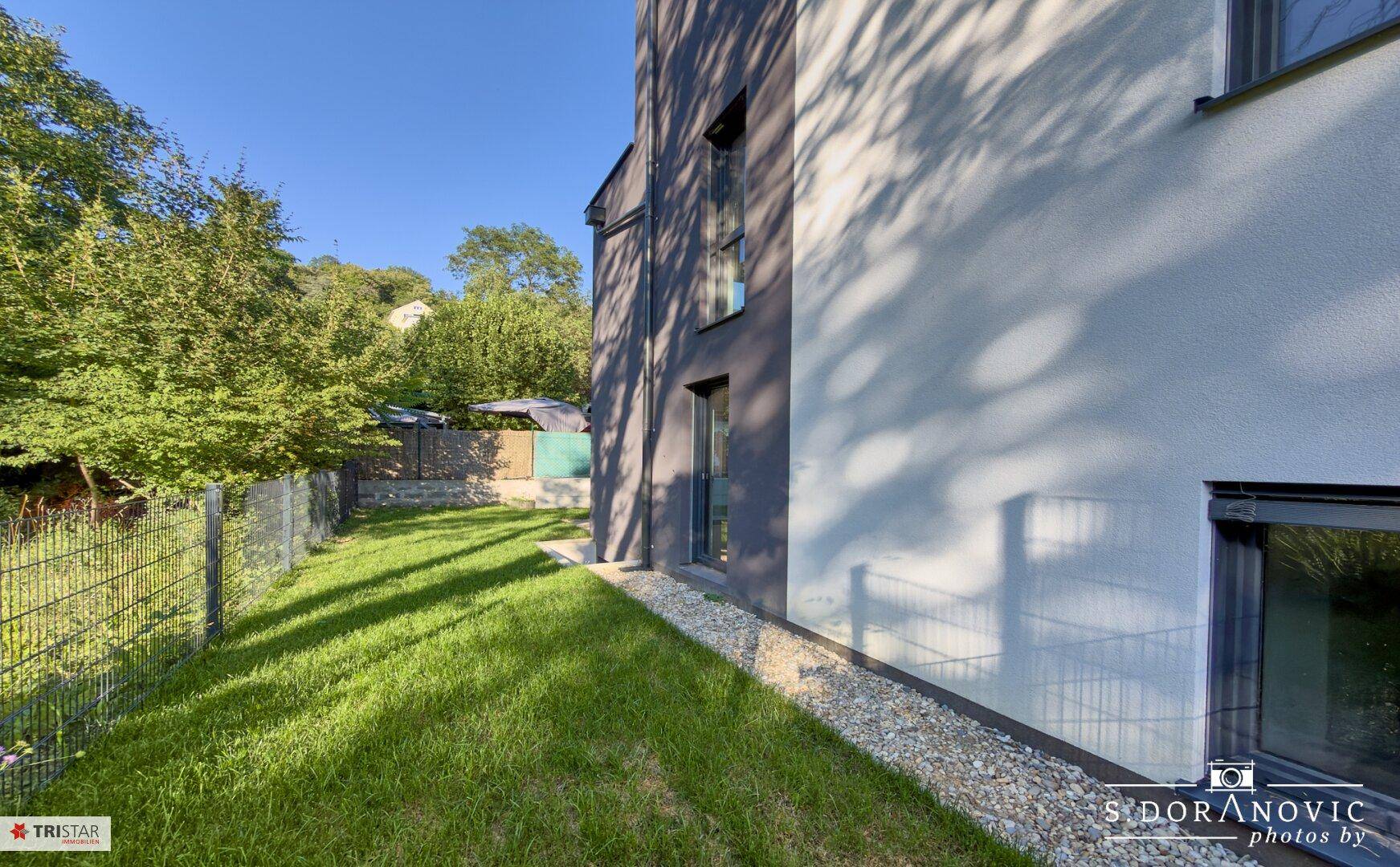 Seitenansicht eines modernen Hauses mit gepflegtem Rasen und einem Kiesstreifen entlang der Fassade.