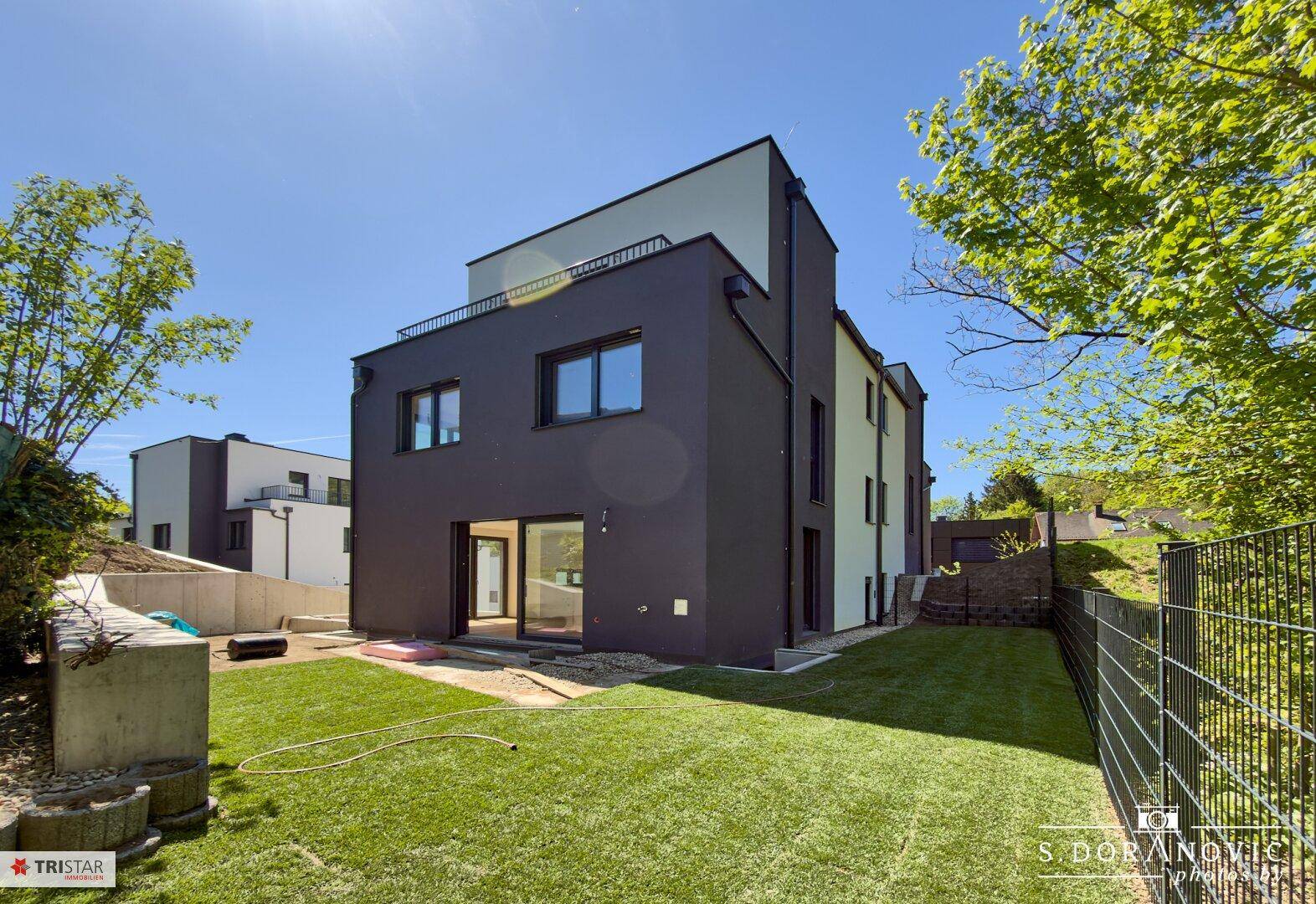 Rückansicht eines modernen Gebäudes mit dunkler Fassade, Rasenfläche und großen Glasfronten.