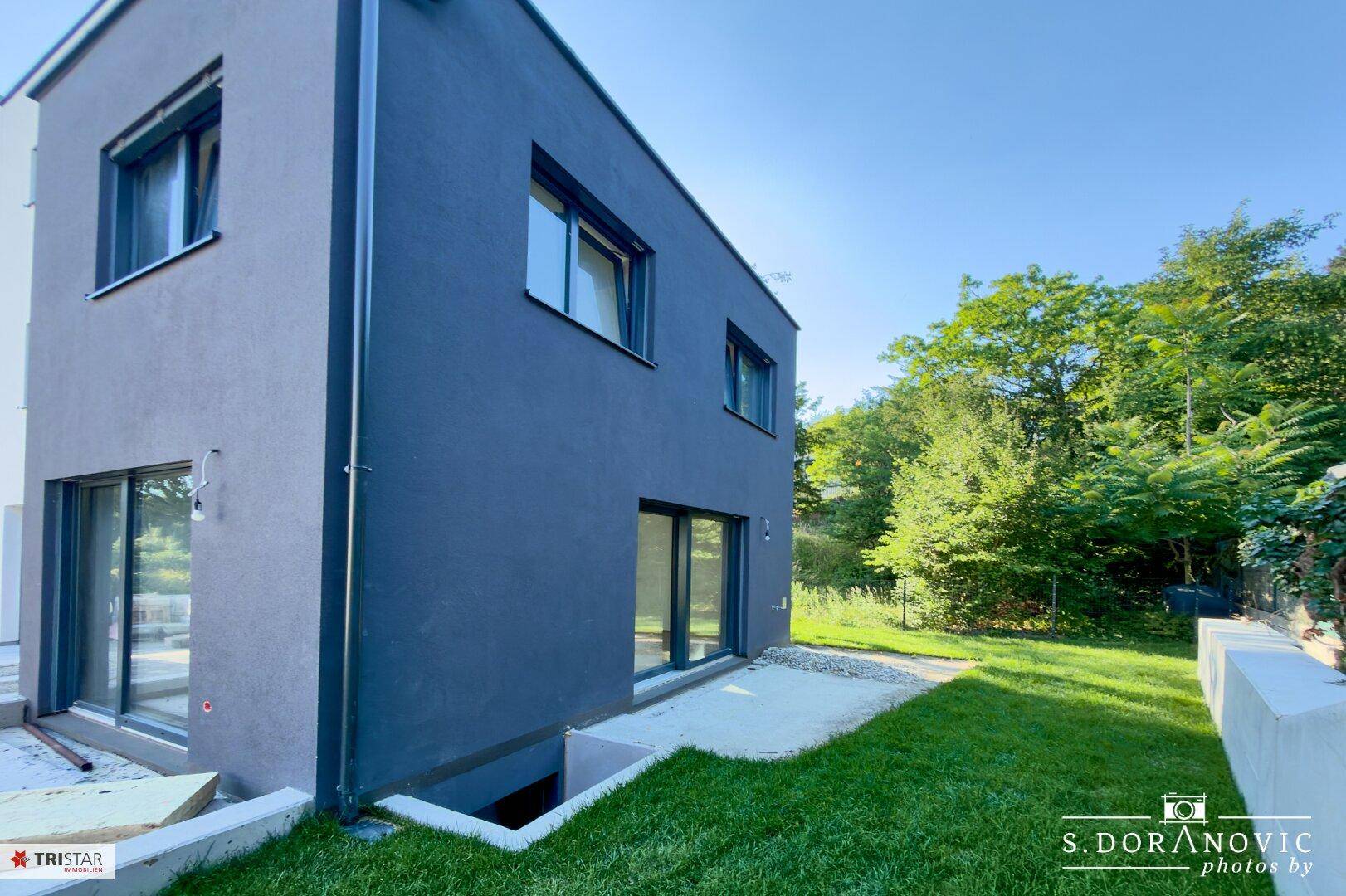 Seitenansicht eines modernen Gebäudes mit dunkler Fassade, Rasenfläche und kleiner Betonfläche.