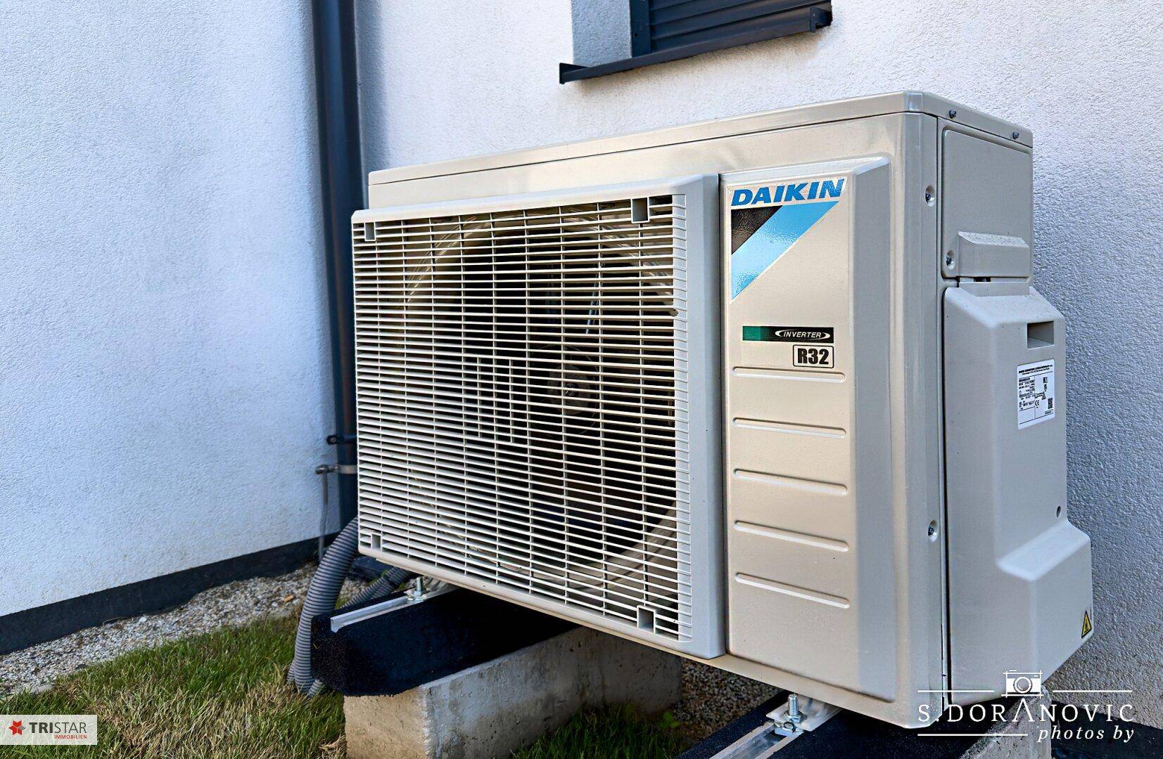 Außenansicht einer modernen Daikin Klimaanlage, installiert neben dem Gebäude auf einer kleinen Grünfläche.