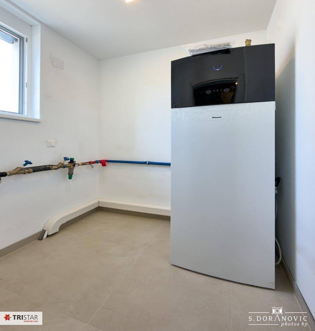 Funktionaler Hauswirtschaftsraum mit moderner Heizungsanlage, Fliesenboden und sichtbaren Installationen.