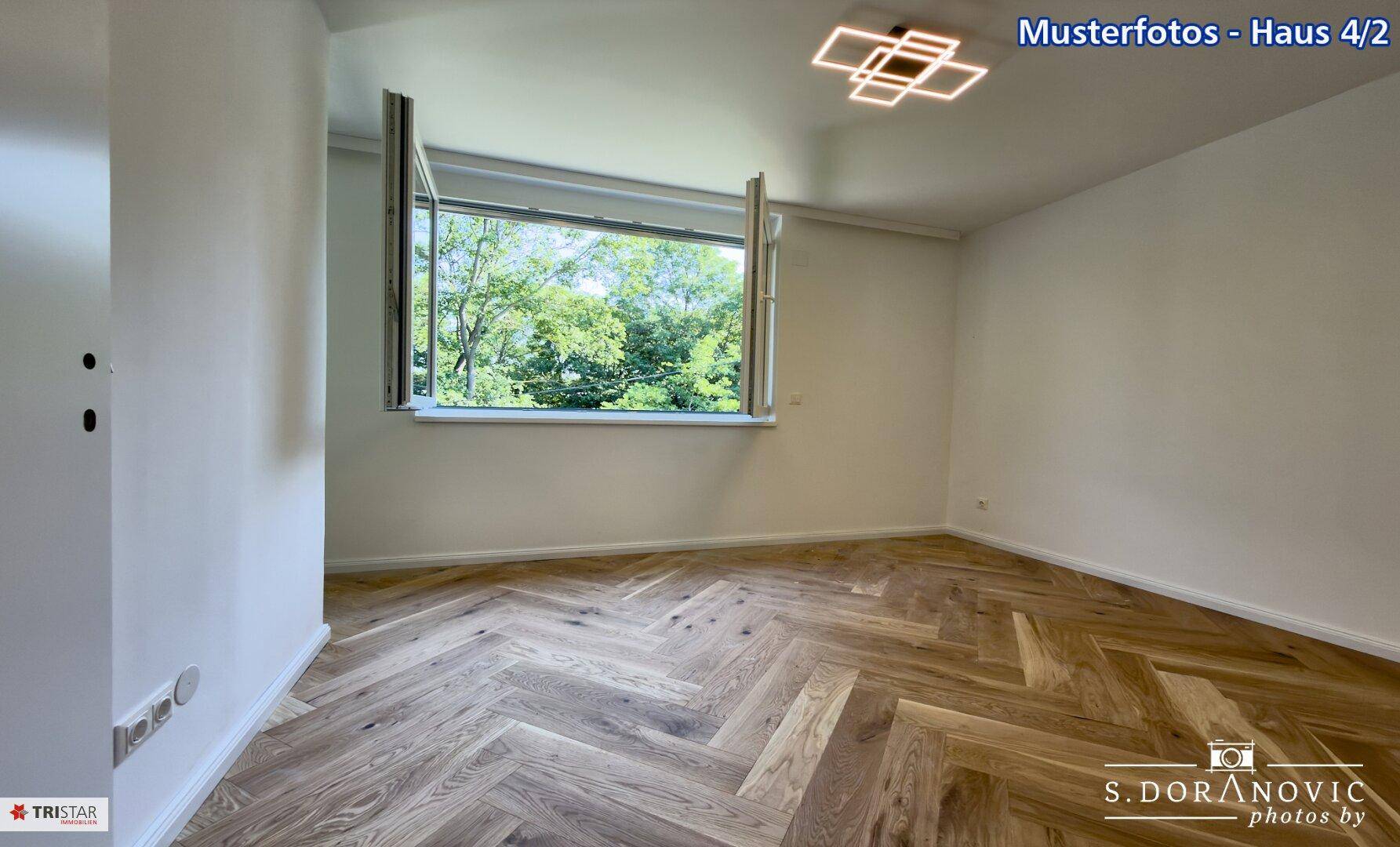 Helles Zimmer mit elegantem Fischgrätparkett und großem Fenster mit Blick ins Grüne.