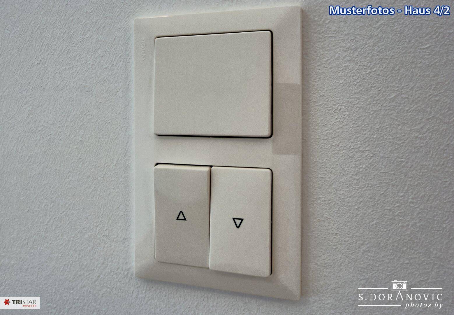 Nahaufnahme eines modernen Lichtschalters und Rollladenbedienfelds an der Wand.