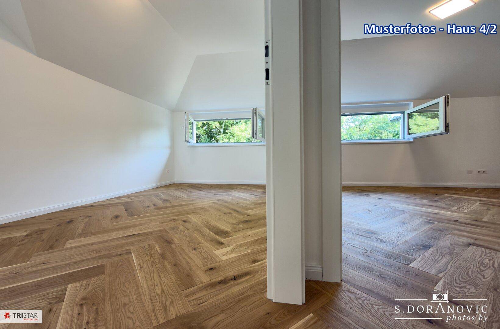 Geräumiges Zimmer im Dachgeschoss mit schrägen Wänden, Fischgrätparkett und Fenstern mit Waldblick.