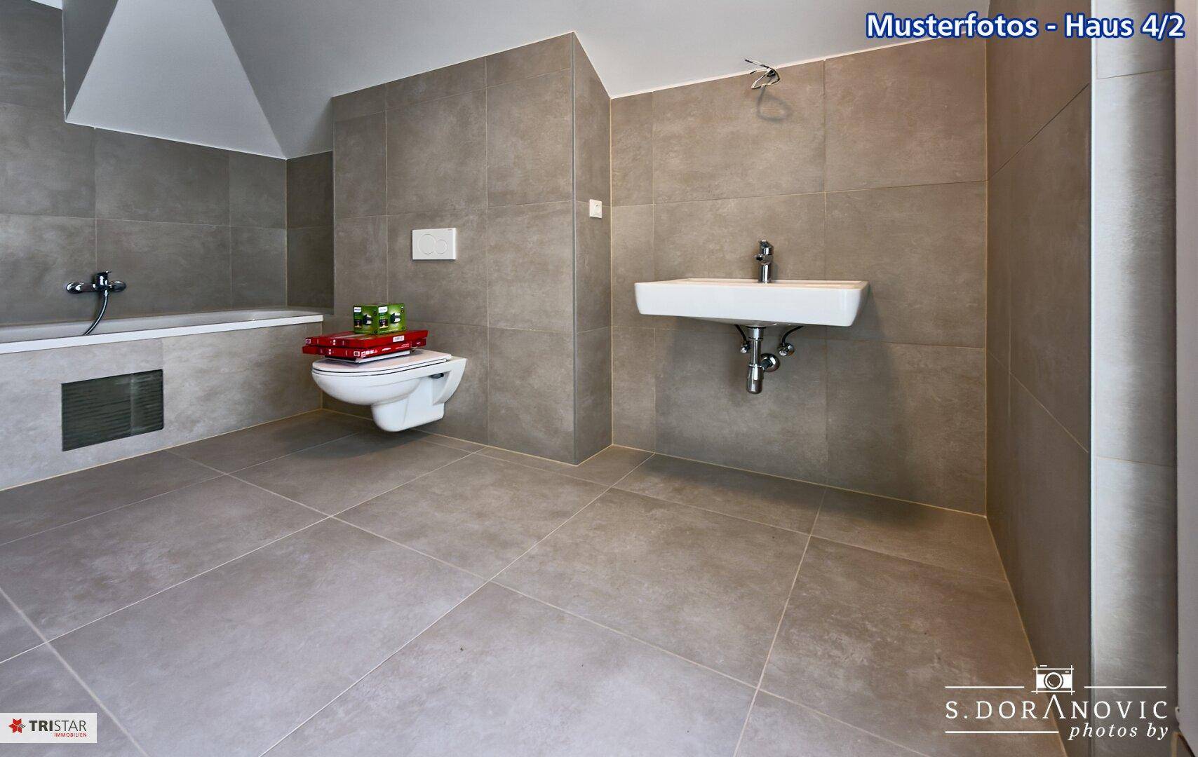 Modernes Badezimmer mit grauen Fliesen, wandhängendem WC und integrierter Badewanne.