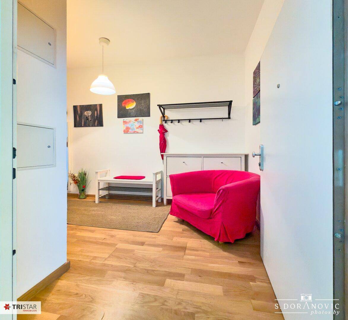 Eingangsbereich mit Holzboden, Garderobe und einem auffälligen pinken Sessel.