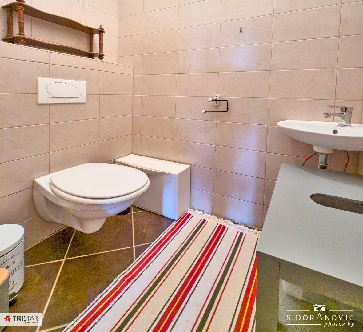 Separate Toilette mit Wand-WC, Waschbecken und beigefarbenen Fliesen.