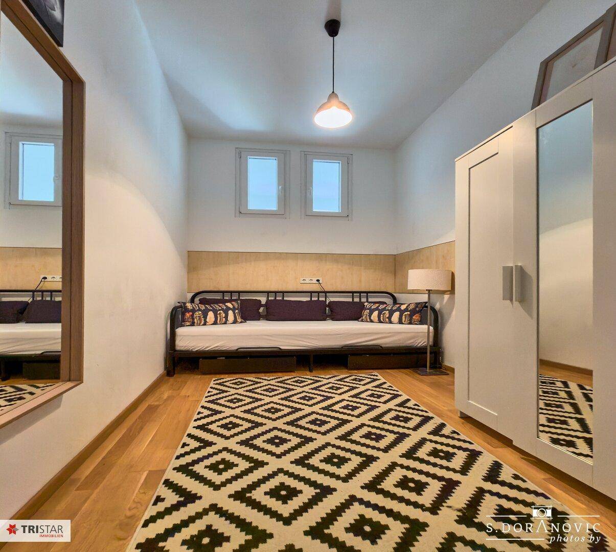 Gemütliches Schlafzimmer mit Holzboden, Tagesbett und modernem Teppichmuster.