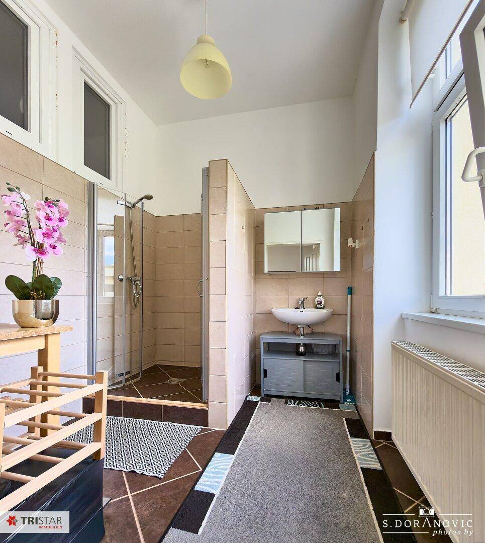 Badezimmer mit Duschkabine, Waschbecken, Spiegelschrank und Fenster für Tageslicht.
