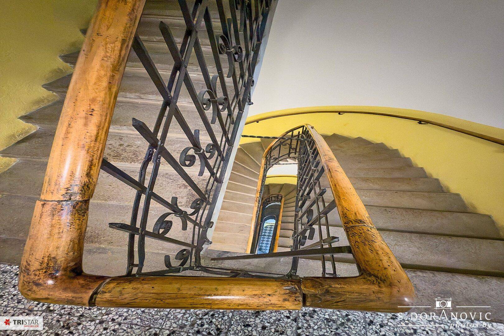 Historisches Treppenhaus mit schmiedeeisernem Geländer und Holzhandlauf, Blick nach unten.