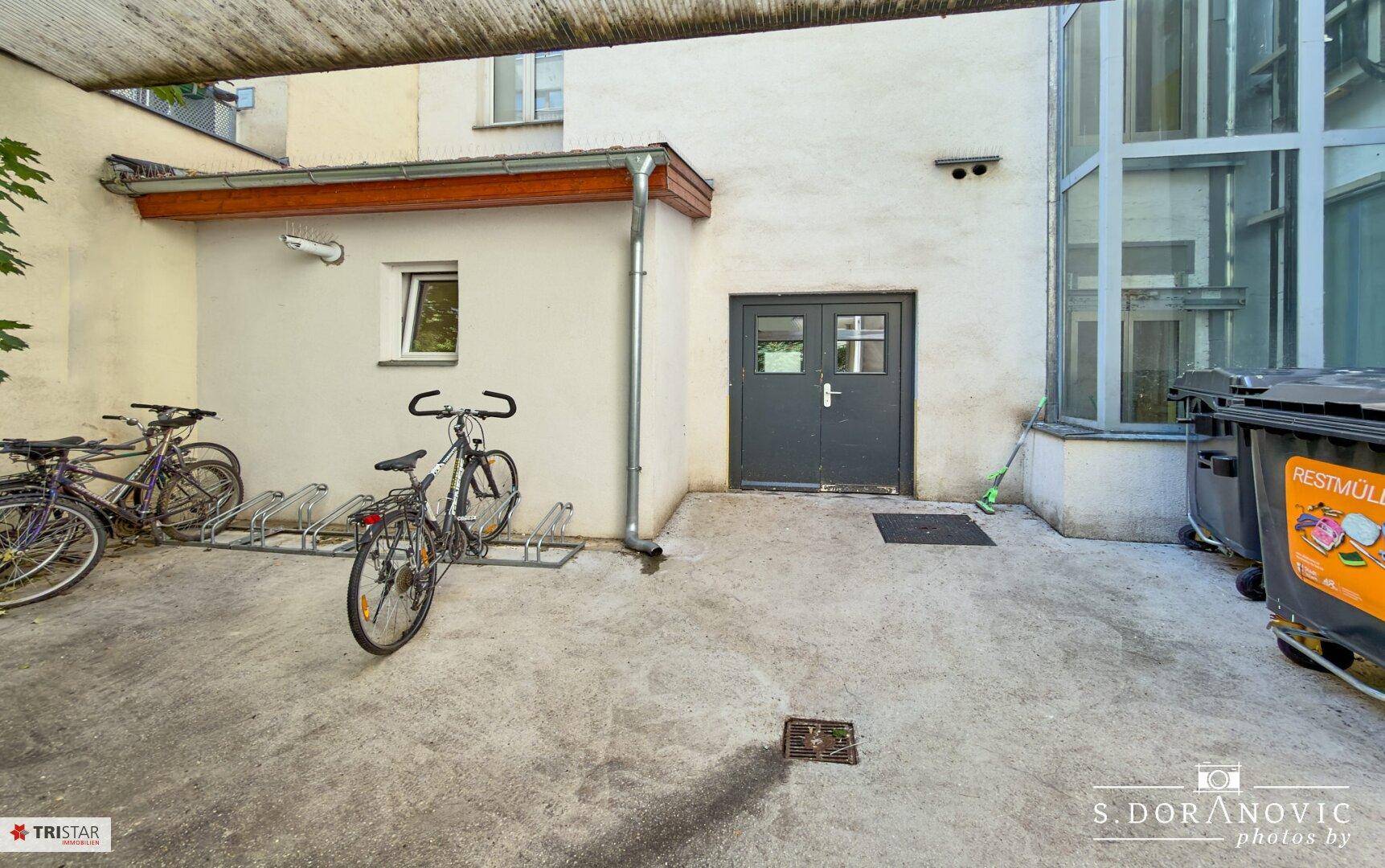 Außenbereich mit Fahrradständern, Mülltonnen und einem Nebengebäude.
