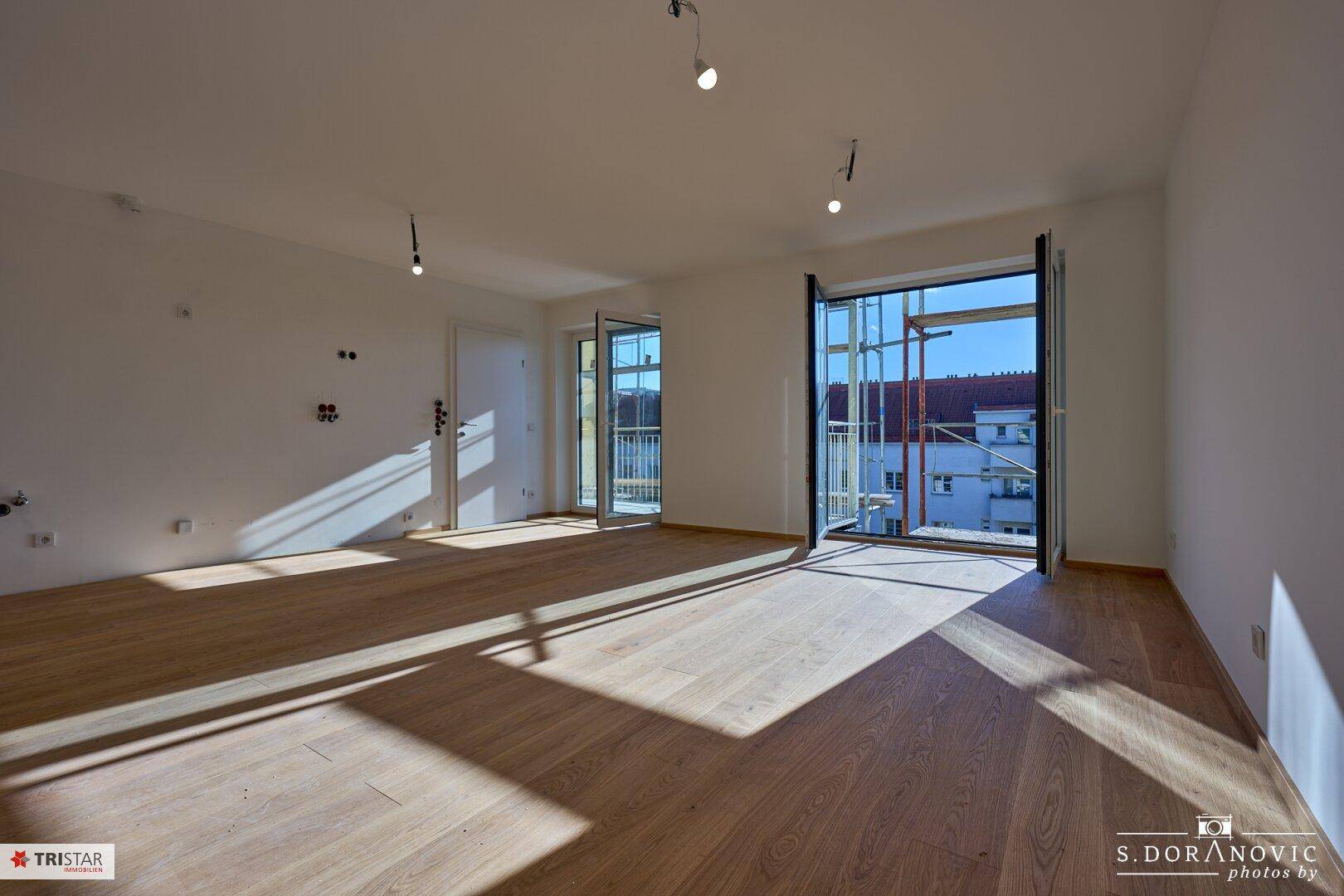 Lichtdurchfluteter Wohnraum mit Holzboden und Zugang zu einem Außenbereich, noch im Bau.