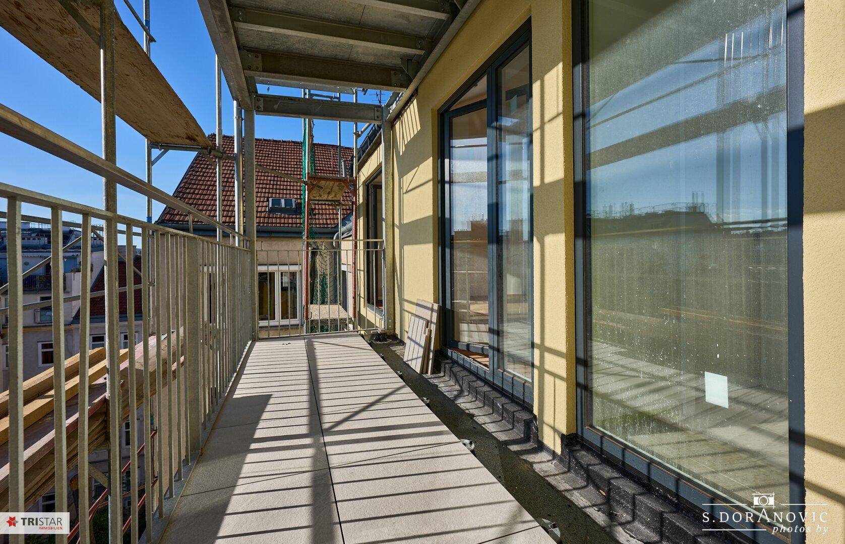 Langer Balkon mit Metallgeländer und Blick auf die umliegenden Gebäude, noch im Bau.