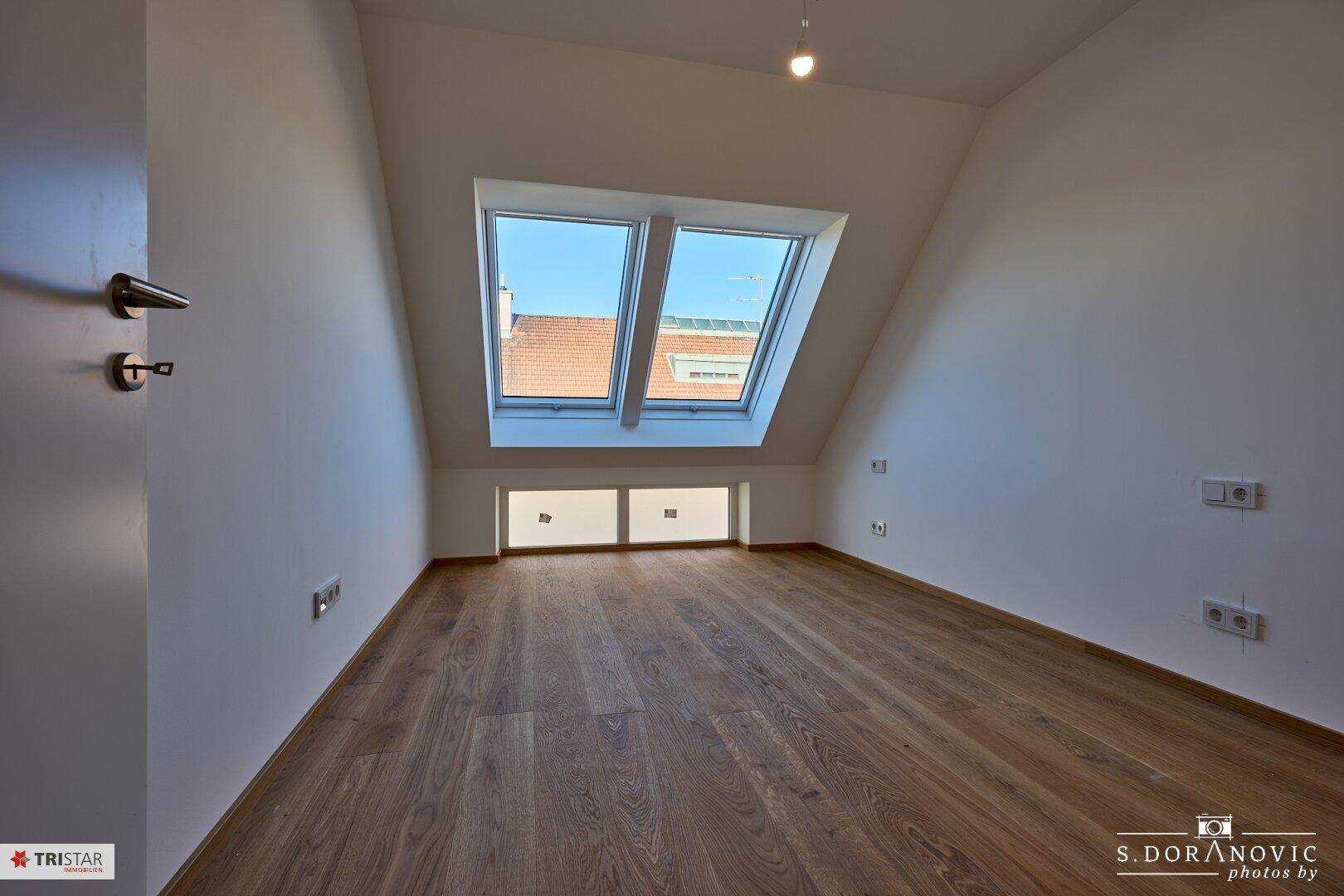 Geräumiges Schlafzimmer im Dachgeschoss mit Holzboden und Dachfenstern.