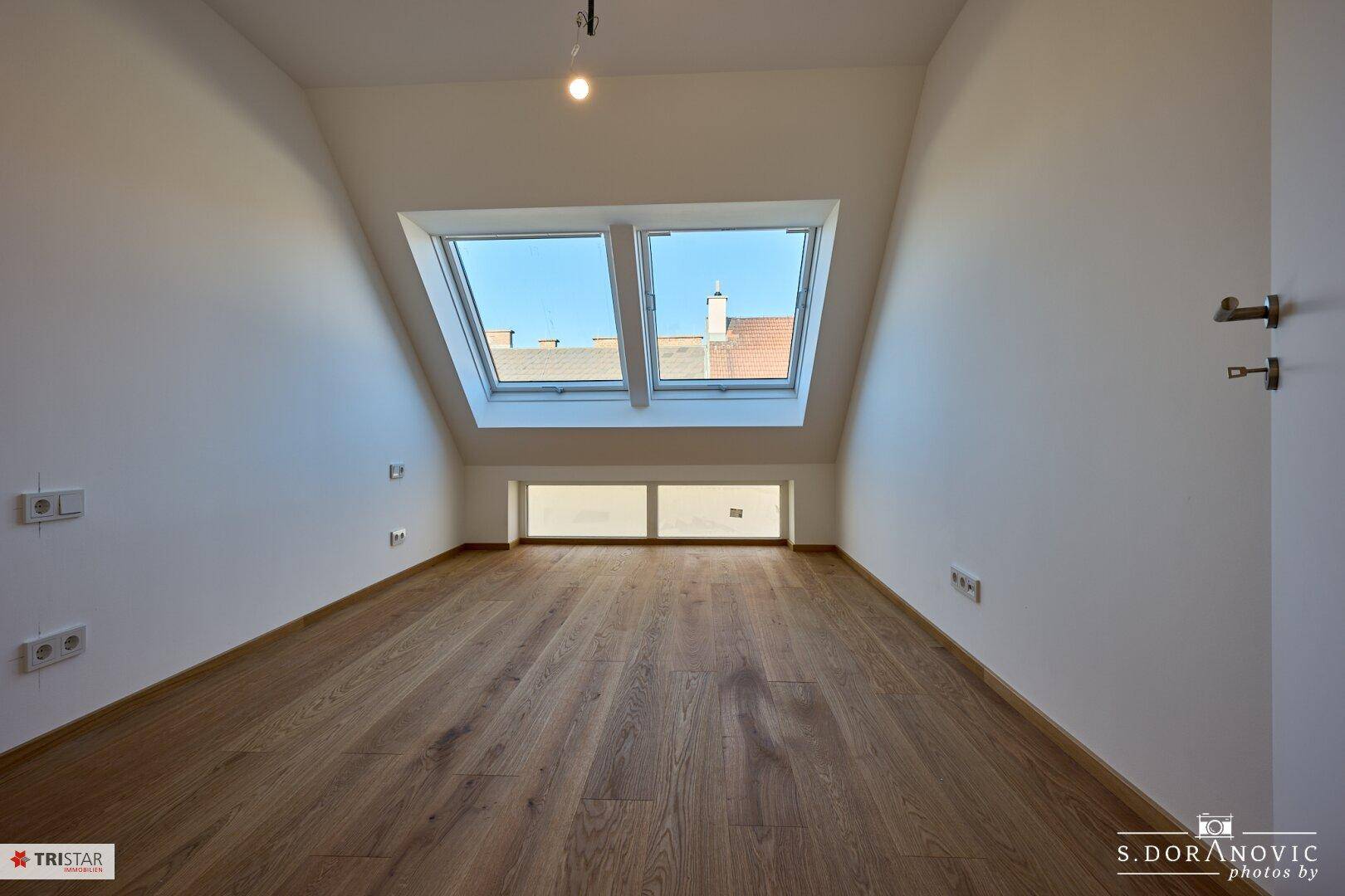 Helles Schlafzimmer im Dachgeschoss mit Holzboden und zwei Dachfenstern.