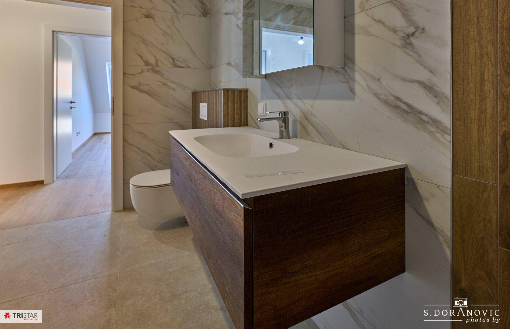Modernes Badezimmer mit schwebendem Waschtisch, Wand-WC und eleganten Marmorfliesen.