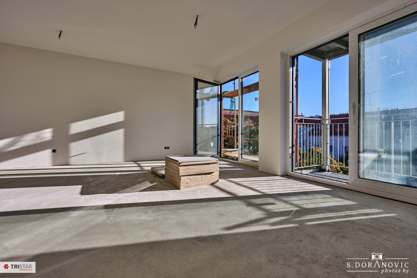 Helles, unfertiges Wohnzimmer mit großen Schiebetüren, die zu einem Balkon führen und viel Tageslicht hereinlassen.