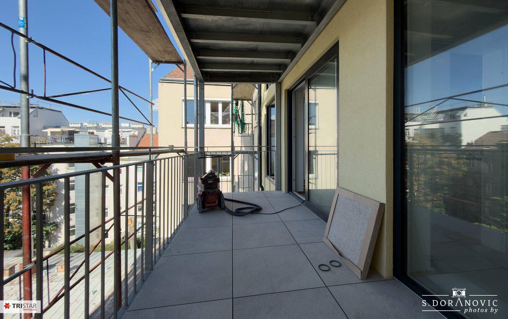 Geräumiger Balkon im Bau mit Fliesenboden und Blick auf die umliegenden Gebäude.