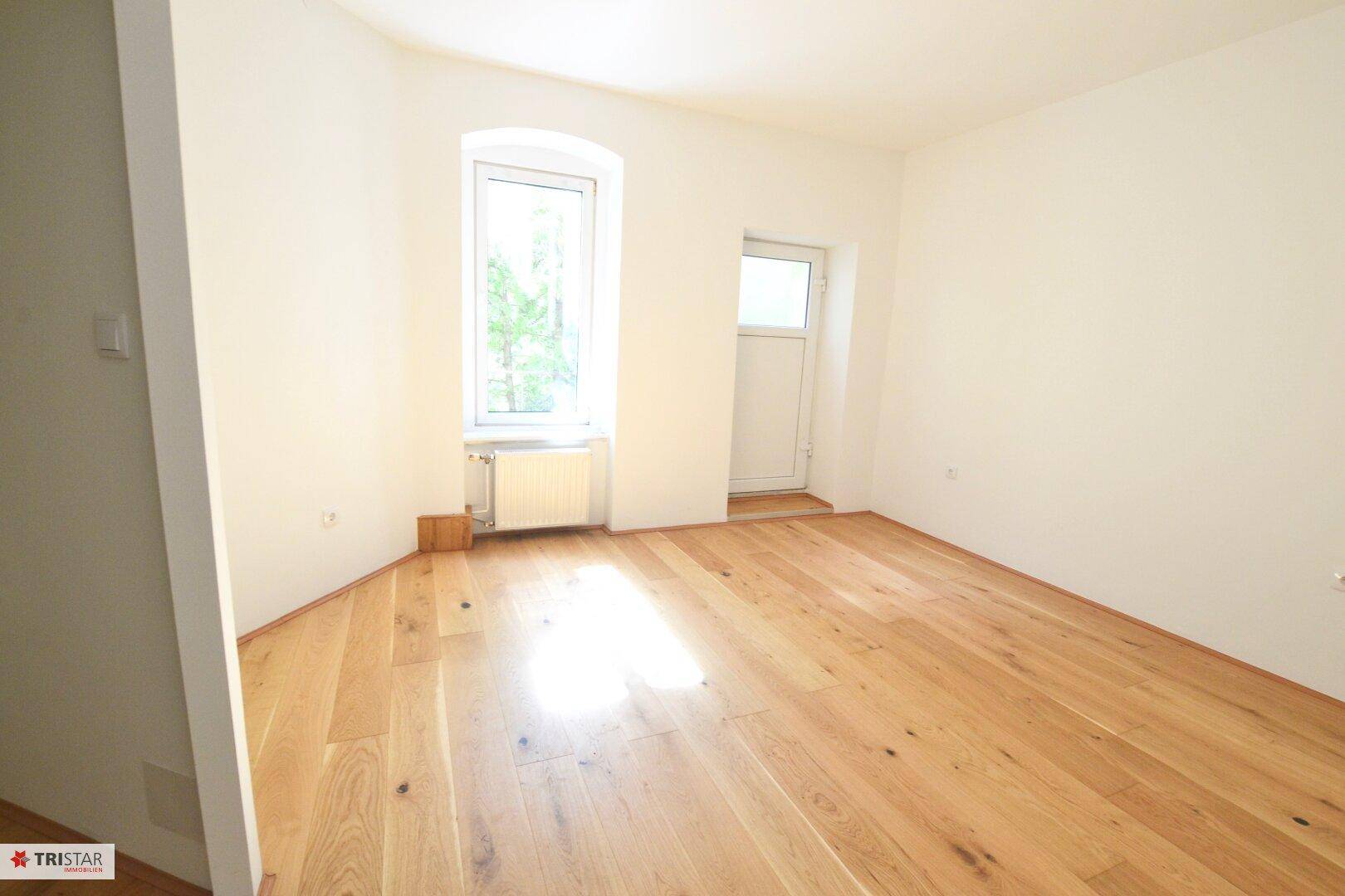 Helles Zimmer mit Holzboden und einem Fenster, das viel Tageslicht hereinlässt.