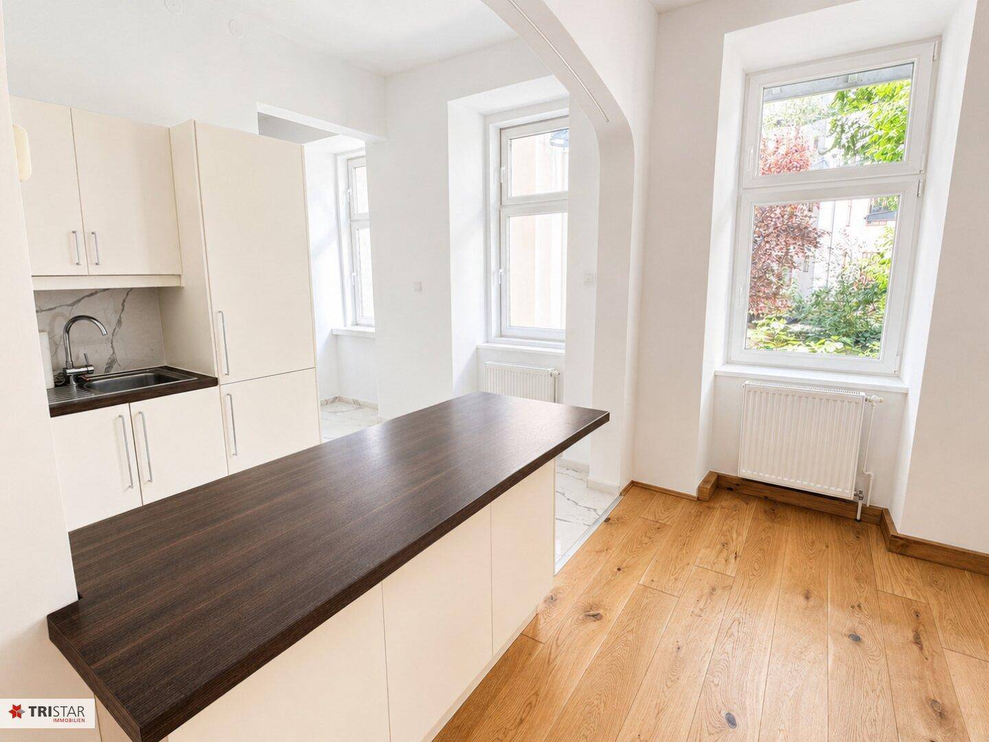 Moderne Küche mit Arbeitsplatte in Holzoptik und Blick ins Grüne durch die Fenster.