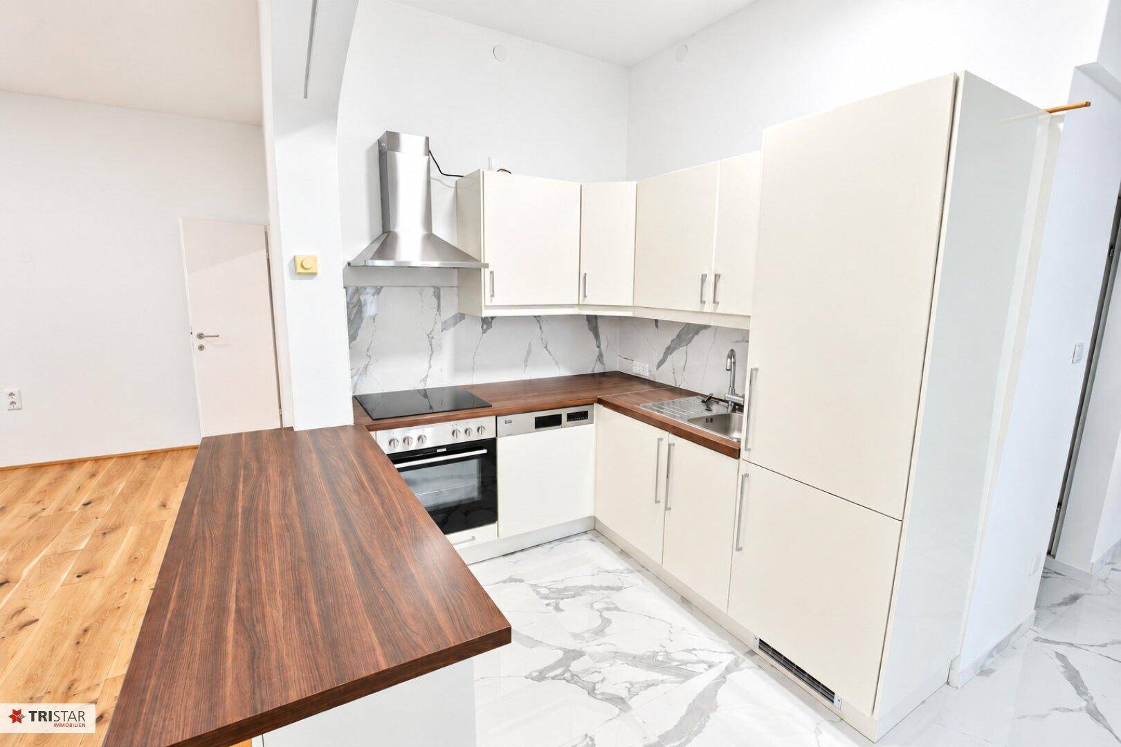 Voll ausgestattete Küche mit weißen Schränken, Holz-Arbeitsplatte und modernen Geräten.
