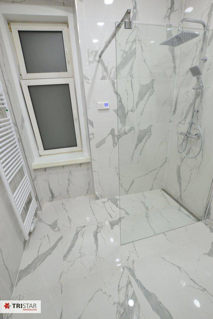 Geräumige Dusche mit Glasabtrennung, Regenduschkopf und Marmorfliesen.
