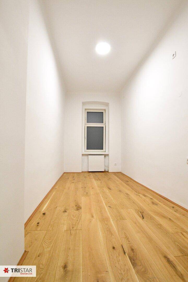 Schmaler Raum mit Holzboden und einem Fenster, das für natürliches Licht sorgt.
