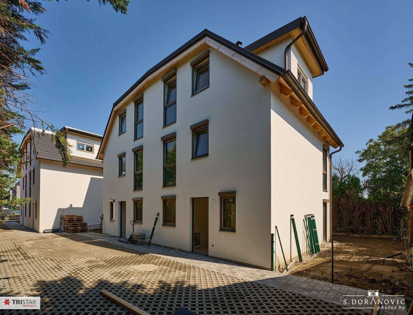 Zwei Neubau-Doppelhaushälften im Rohbau mit gepflasterter Fläche und Baustellenumgebung.
