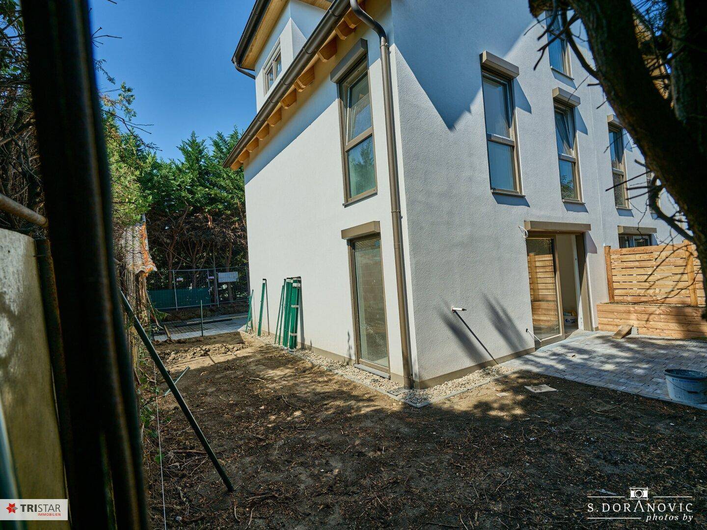 Moderne Hausfassade mit weißem Putz, großen Fenstern und einem unfertigen Gartenbereich.