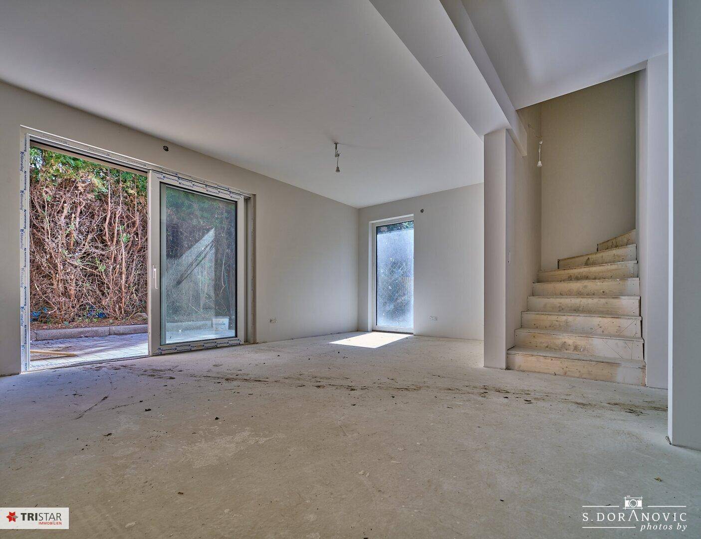 Heller, unfertiger Wohnbereich mit Zugang zur Terrasse und einer Treppe zum Obergeschoss.
