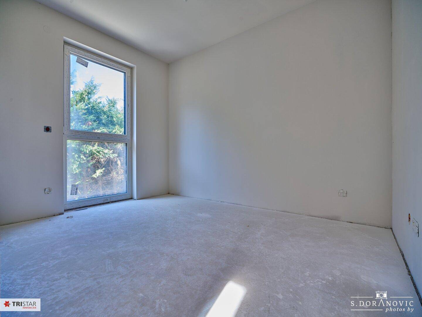 Helles Schlafzimmer im Rohbau mit großem Fenster und Blick ins Grüne.