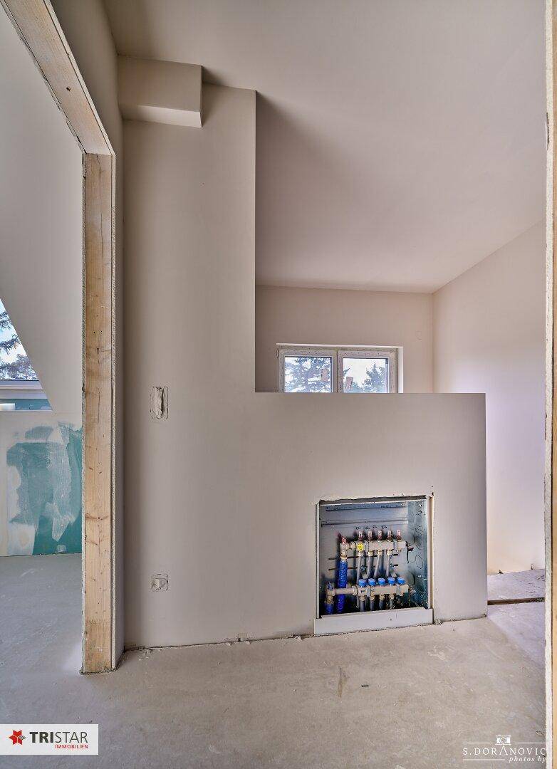 Unfertiger Raum mit sichtbaren Heizungsverteilern und einem Fenster.