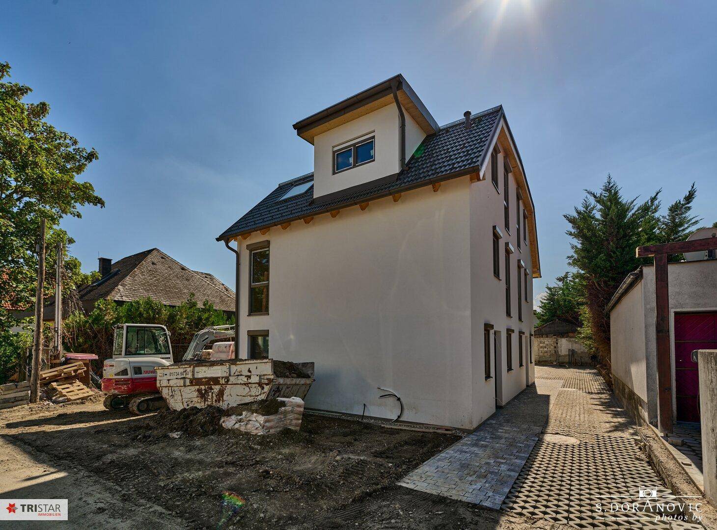 Rückansicht der Neubau-Doppelhaushälfte mit Dachgaube und Baustellenfahrzeug im Gartenbereich.