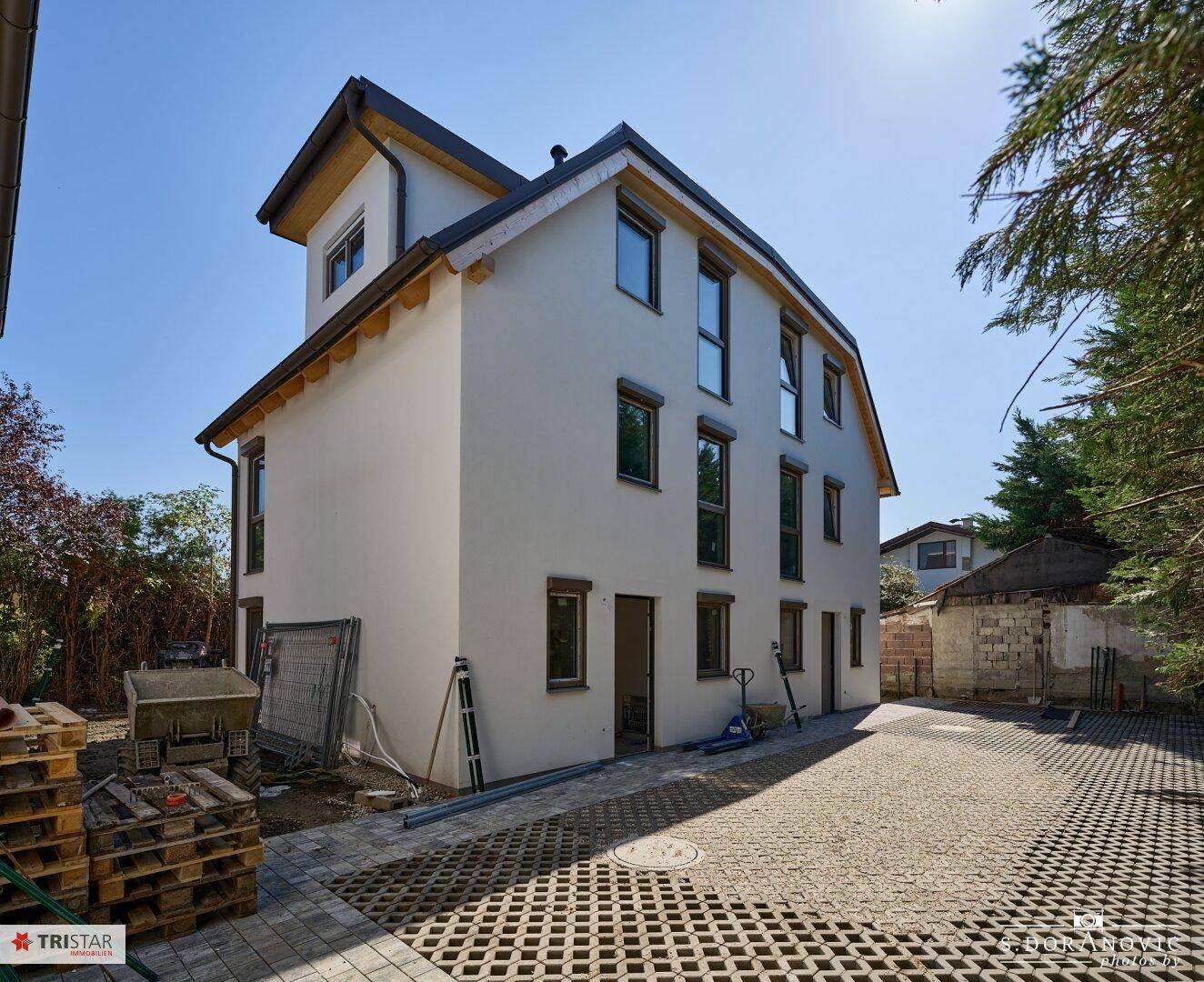Moderne Doppelhaushälfte im Bau mit weißer Fassade und vorbereitetem Außenbereich.