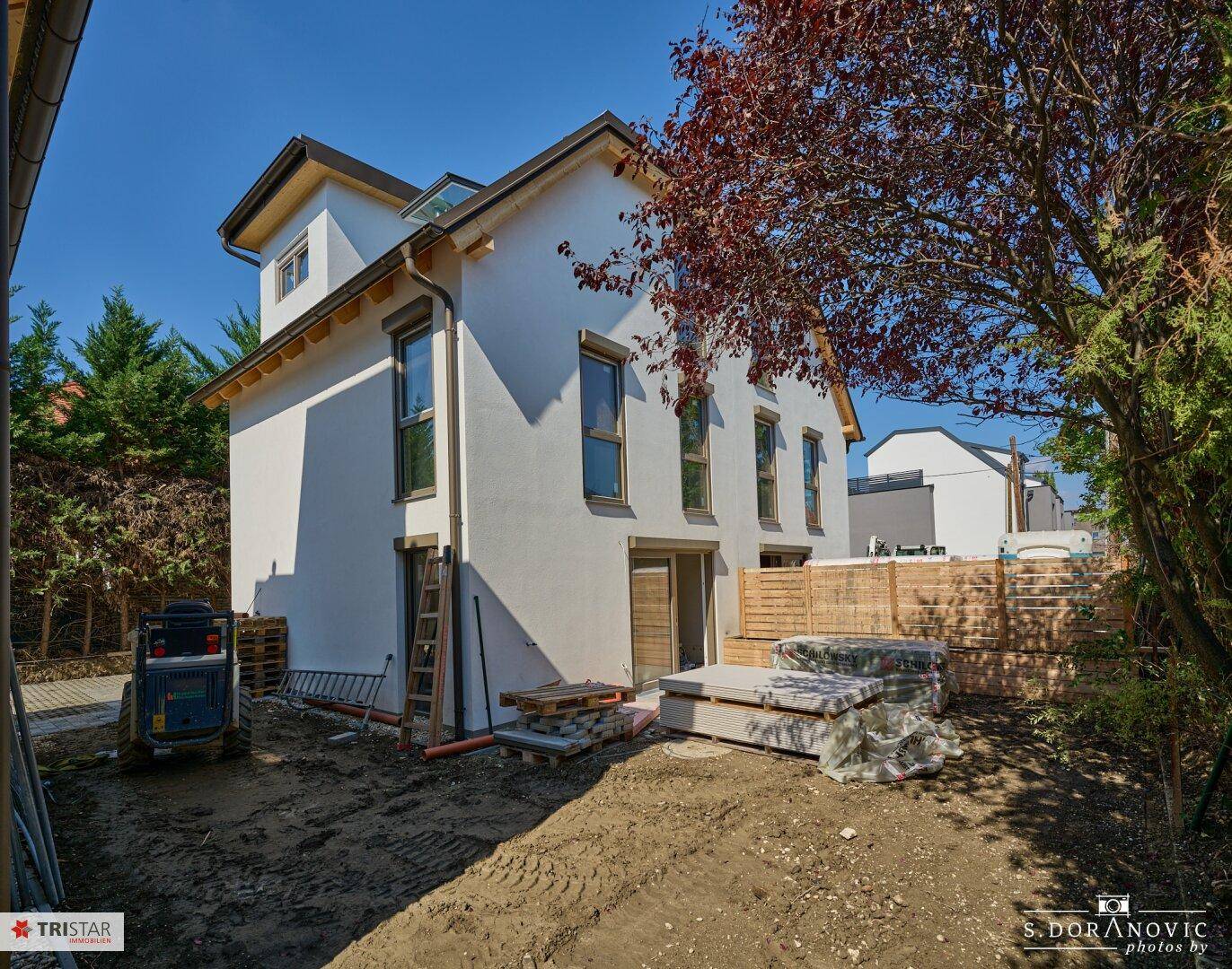 Rückansicht der Doppelhaushälfte mit Gartenbereich in Bau und großen Fenstern.