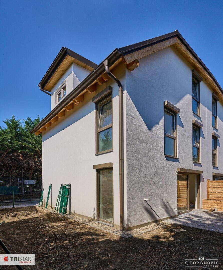 Neubau-Doppelhaushälfte mit weißer Fassade und großen Fenstern, umgeben von Grün.