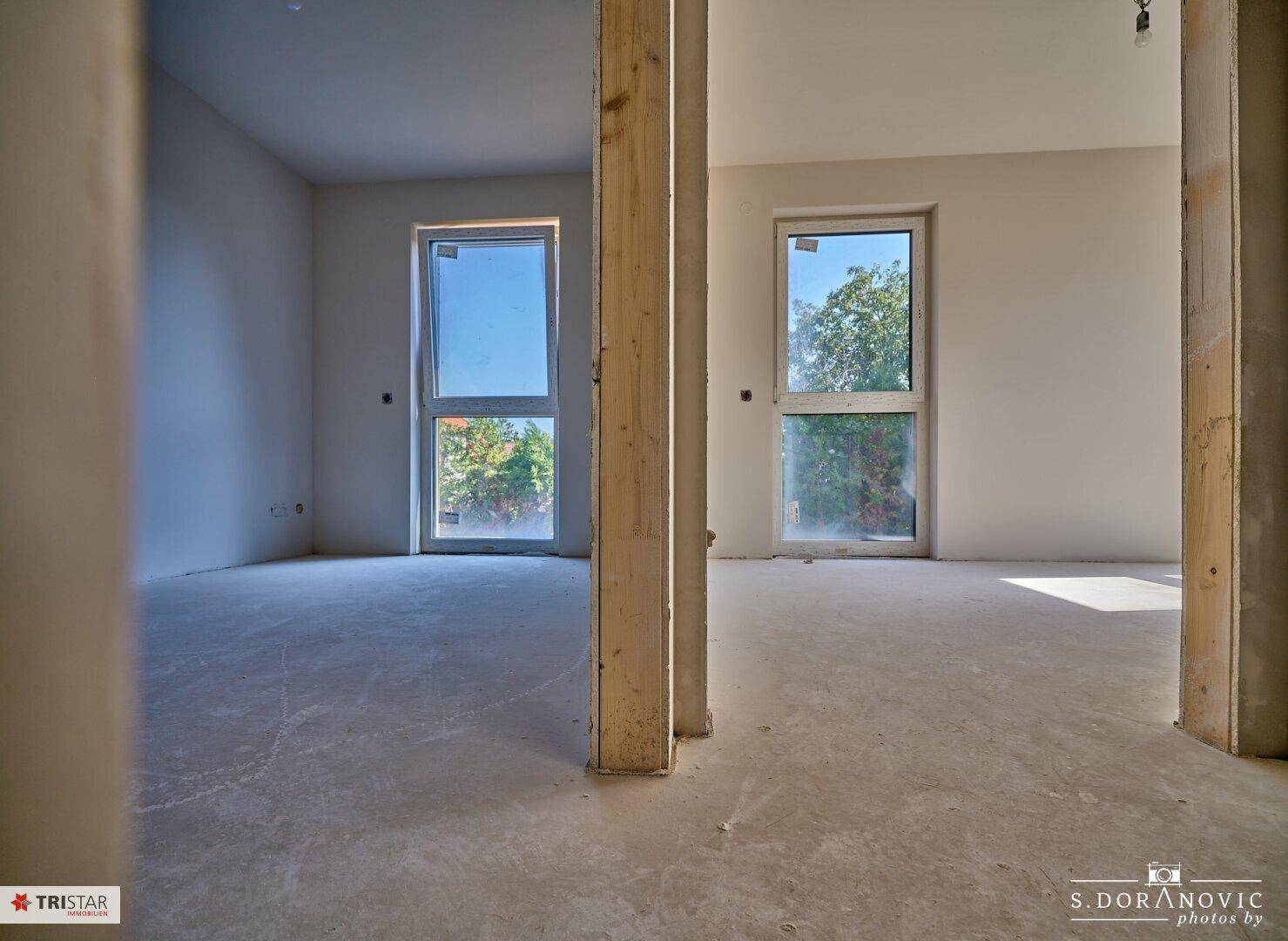 Geräumiges Schlafzimmer im Rohbau mit zwei großen Fenstern und viel Tageslicht.
