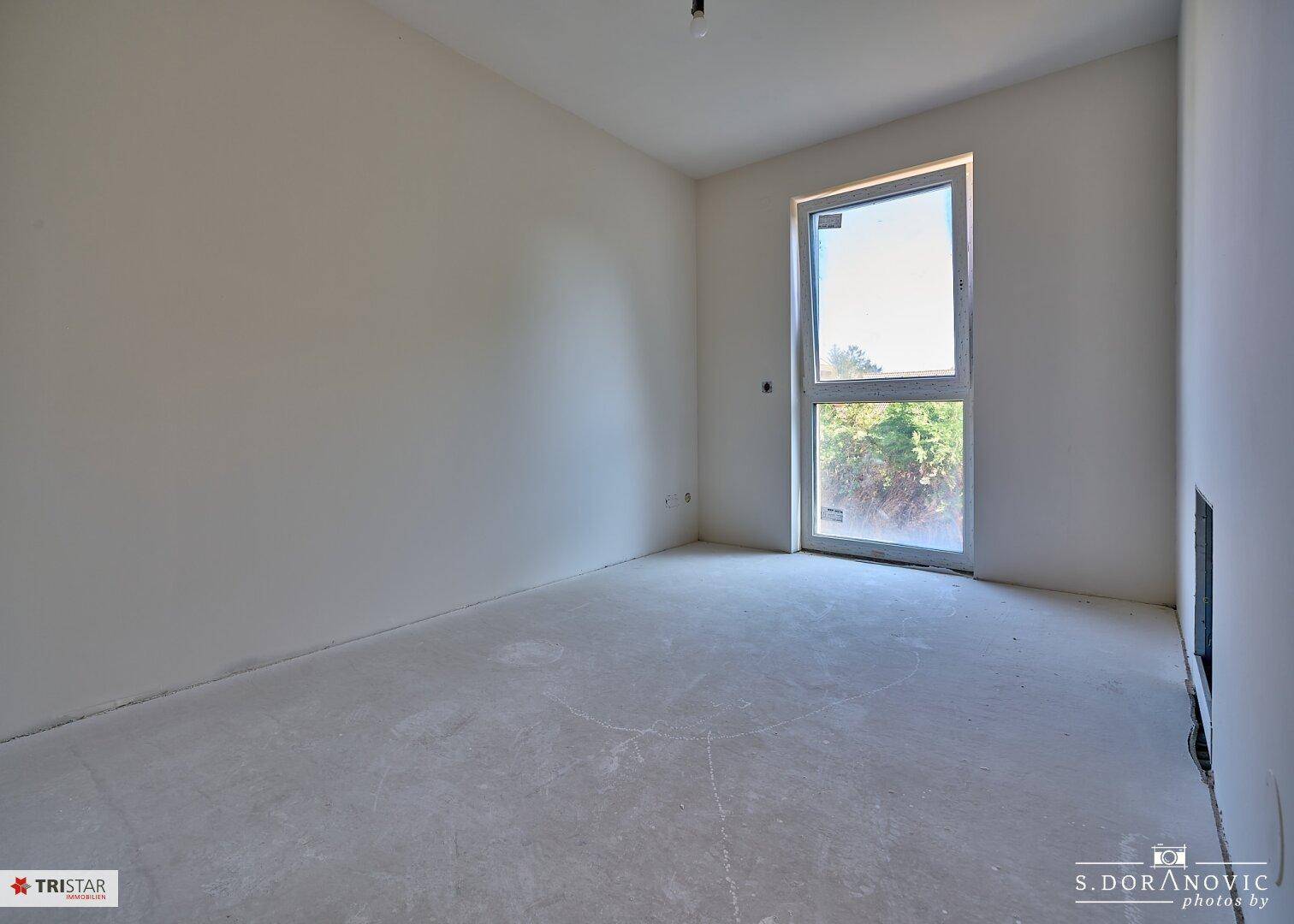 Helles Schlafzimmer im Rohbau mit großem Fenster und Blick ins Grüne.