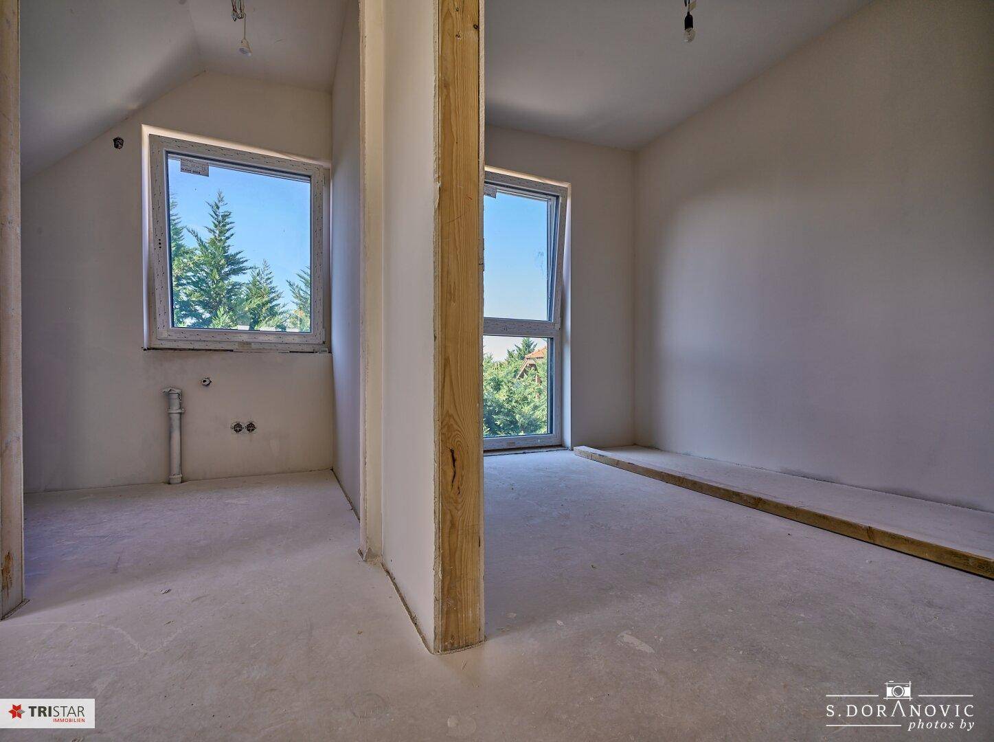 Geräumiges Schlafzimmer im Rohbau mit zwei Fenstern und Blick ins Grüne.
