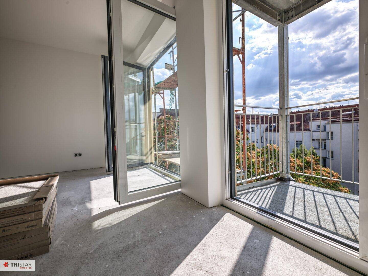 Heller Innenraum mit großen Fenstern und direktem Zugang zu einem Balkon mit Baugerüst.