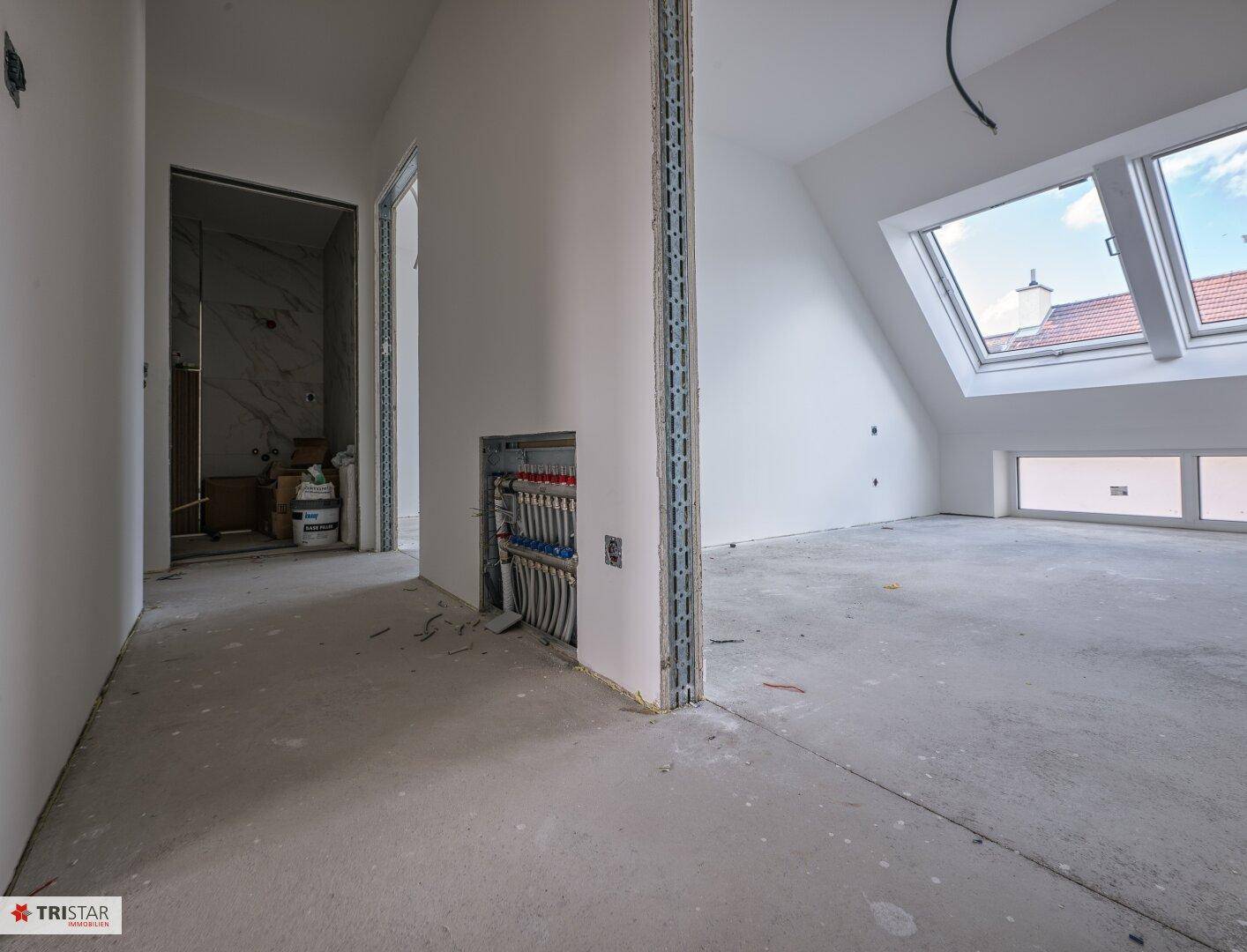 Dachgeschossraum mit schräger Decke, Dachfenstern und Blick auf den angrenzenden, unfertigen Bereich.