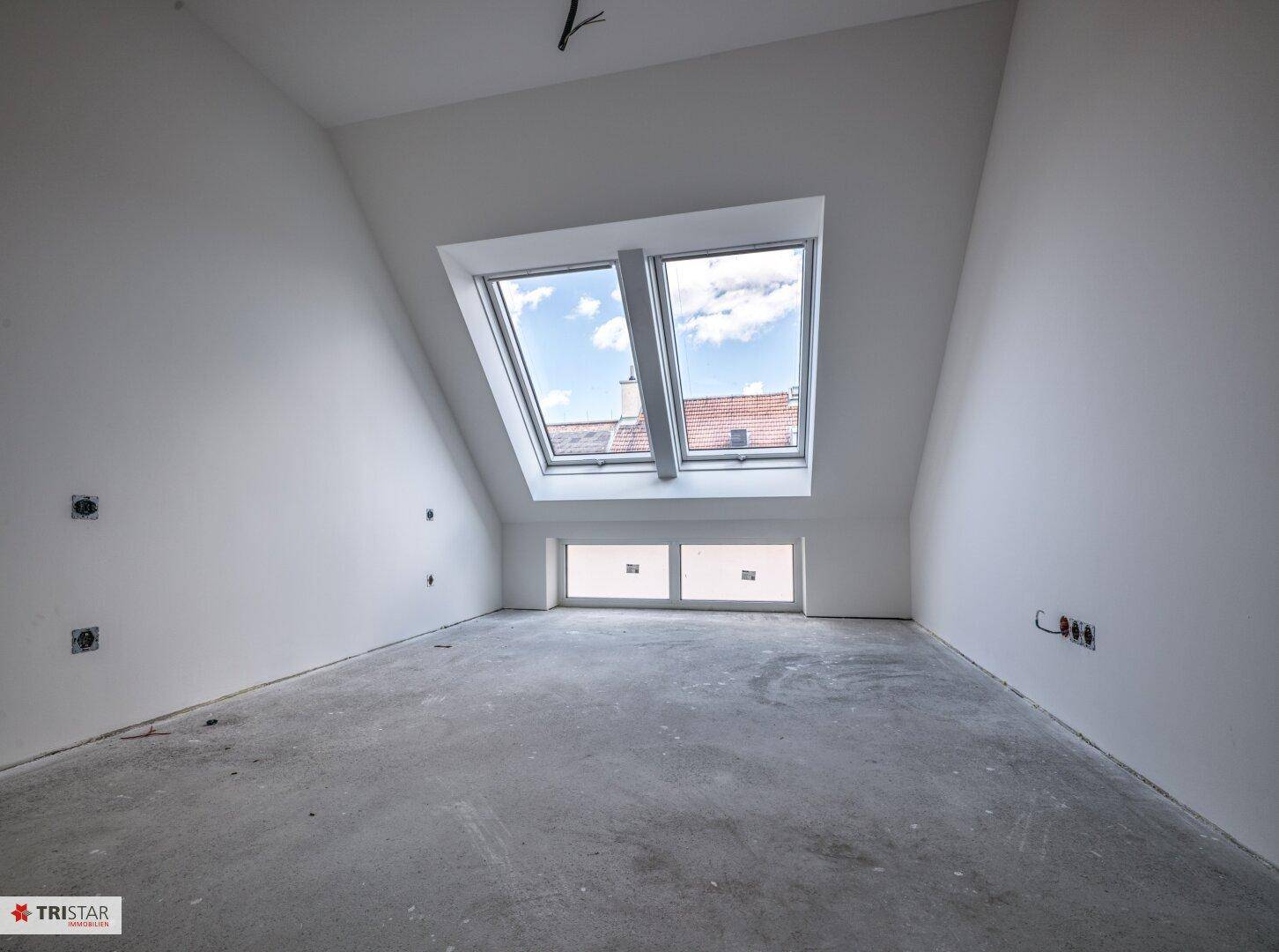 Heller Dachgeschossraum im Rohbau mit schräger Decke und zwei großen Dachfenstern, die viel Licht spenden.
