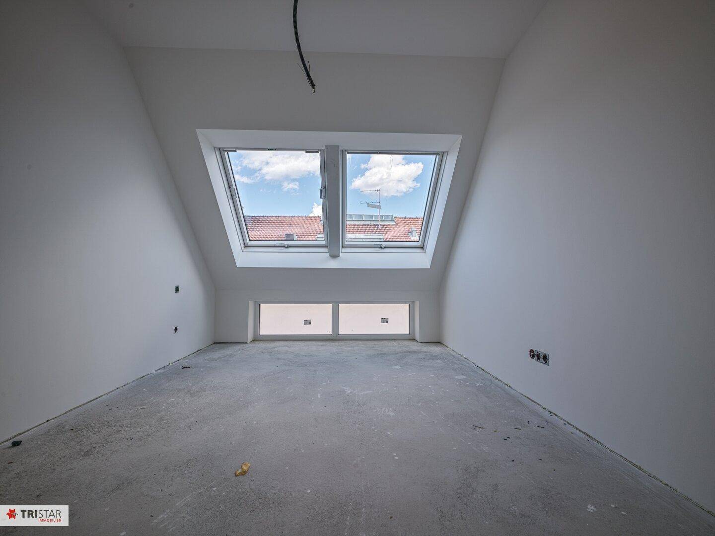 Geräumiger Dachgeschossraum mit viel Tageslicht durch große Dachfenster und schräge Wände.