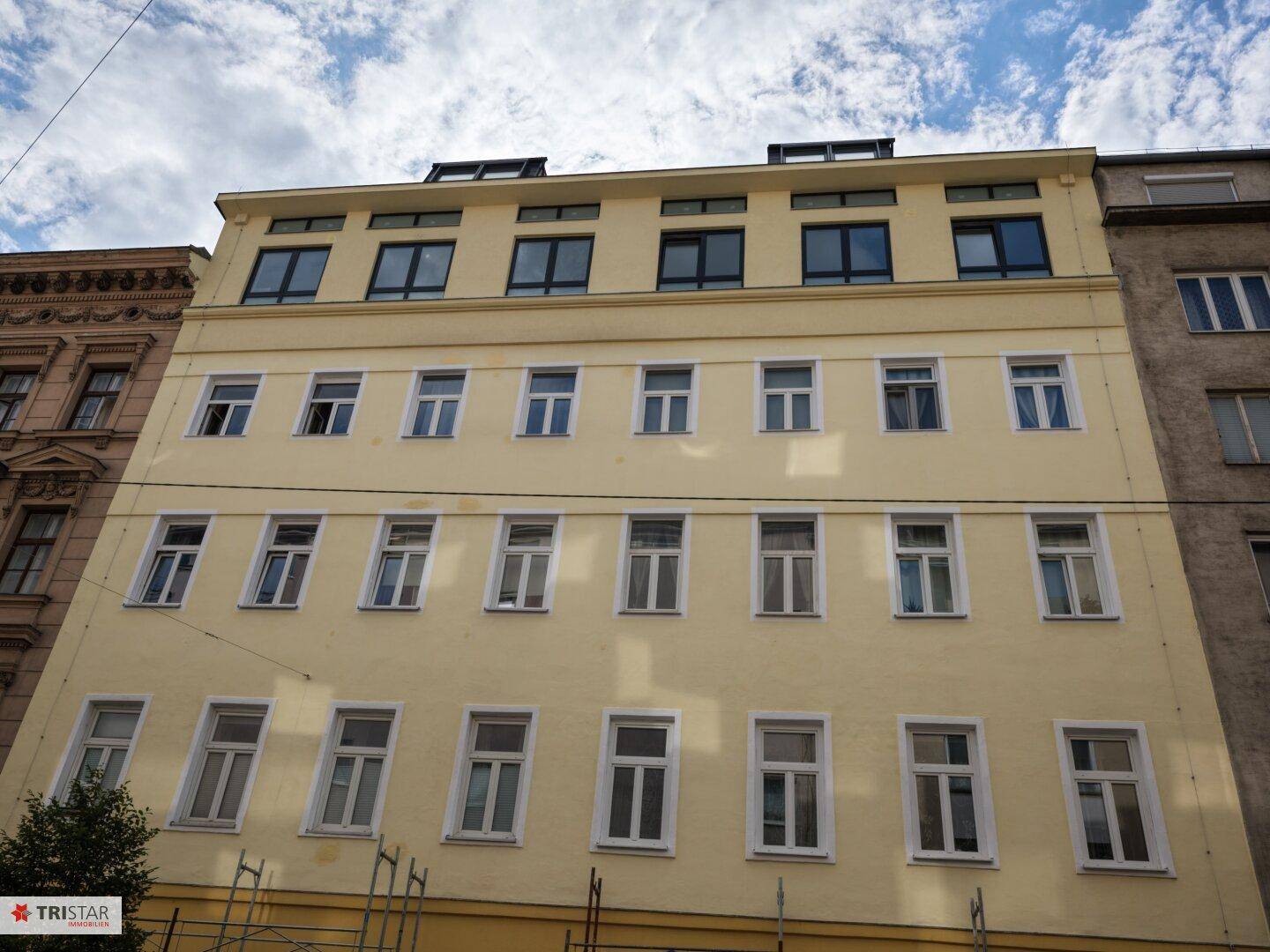 Renovierte gelbe Fassade eines Mehrfamilienhauses mit vielen Fenstern und Flachdach.