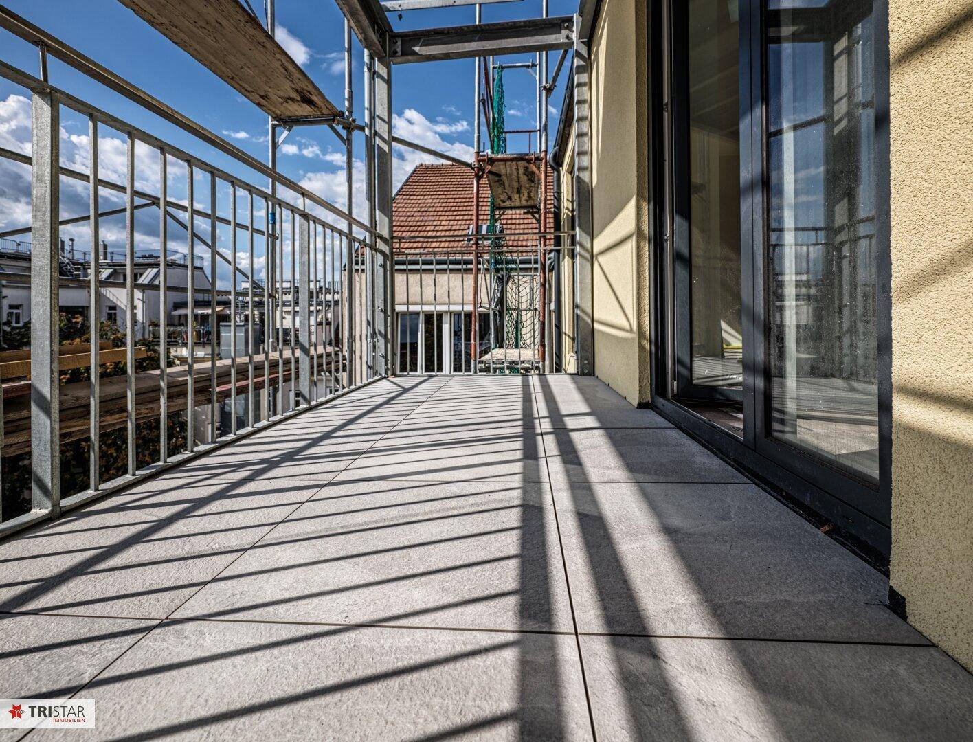 Geräumiger Balkon mit modernen Fliesen und Metallgeländer, noch im Bau, mit viel Sonnenlicht.