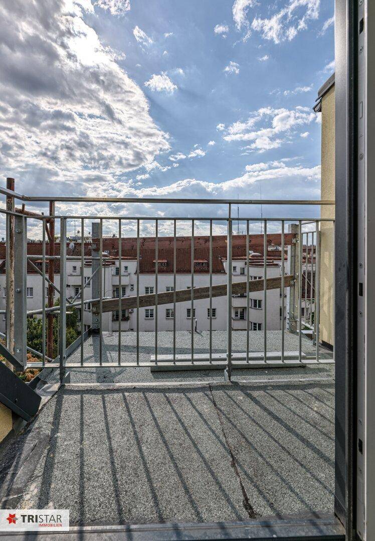 Balkon im Bau mit dunklem Bodenbelag und Metallgeländer, bietet einen Blick auf die Stadt.