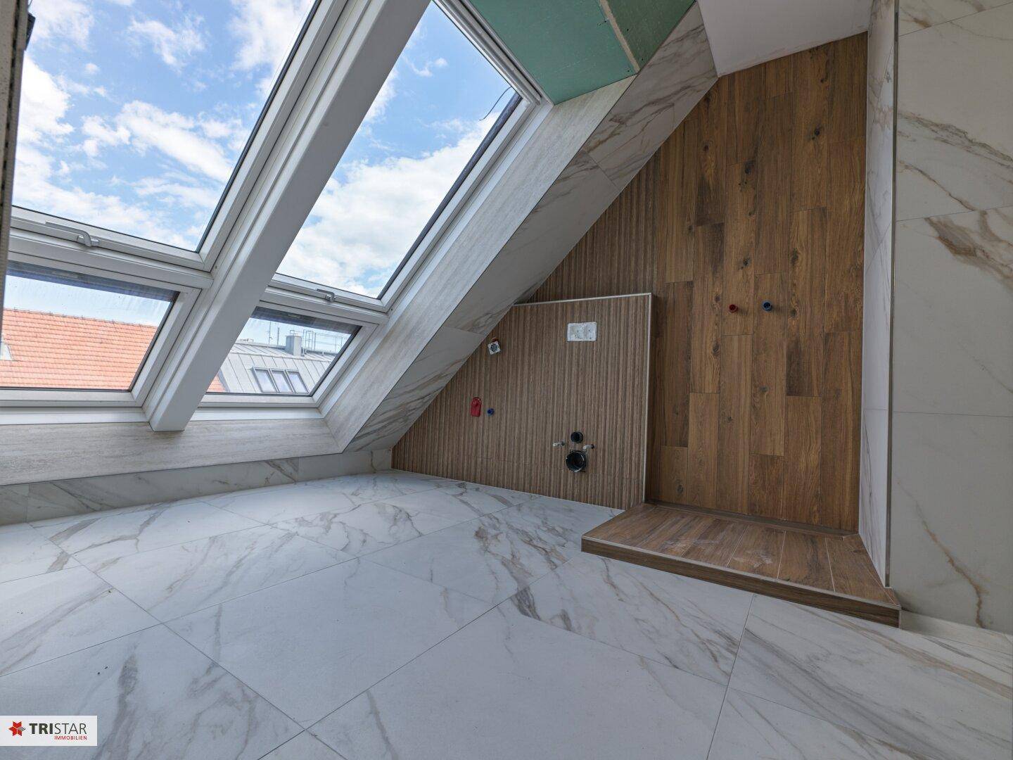 Badezimmer im Bau mit Marmoroptik-Fliesen, Holzpaneelen und zwei großen Dachfenstern unter der Schräge.
