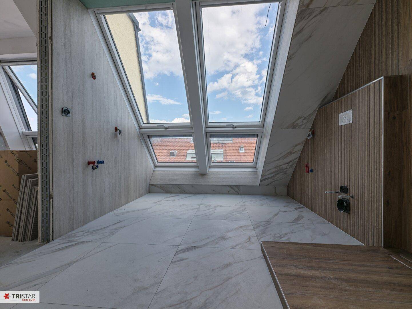Badezimmer im Bau mit Marmoroptik-Fliesen, Holzpaneelen und zwei großen Dachfenstern, die den Raum erhellen.